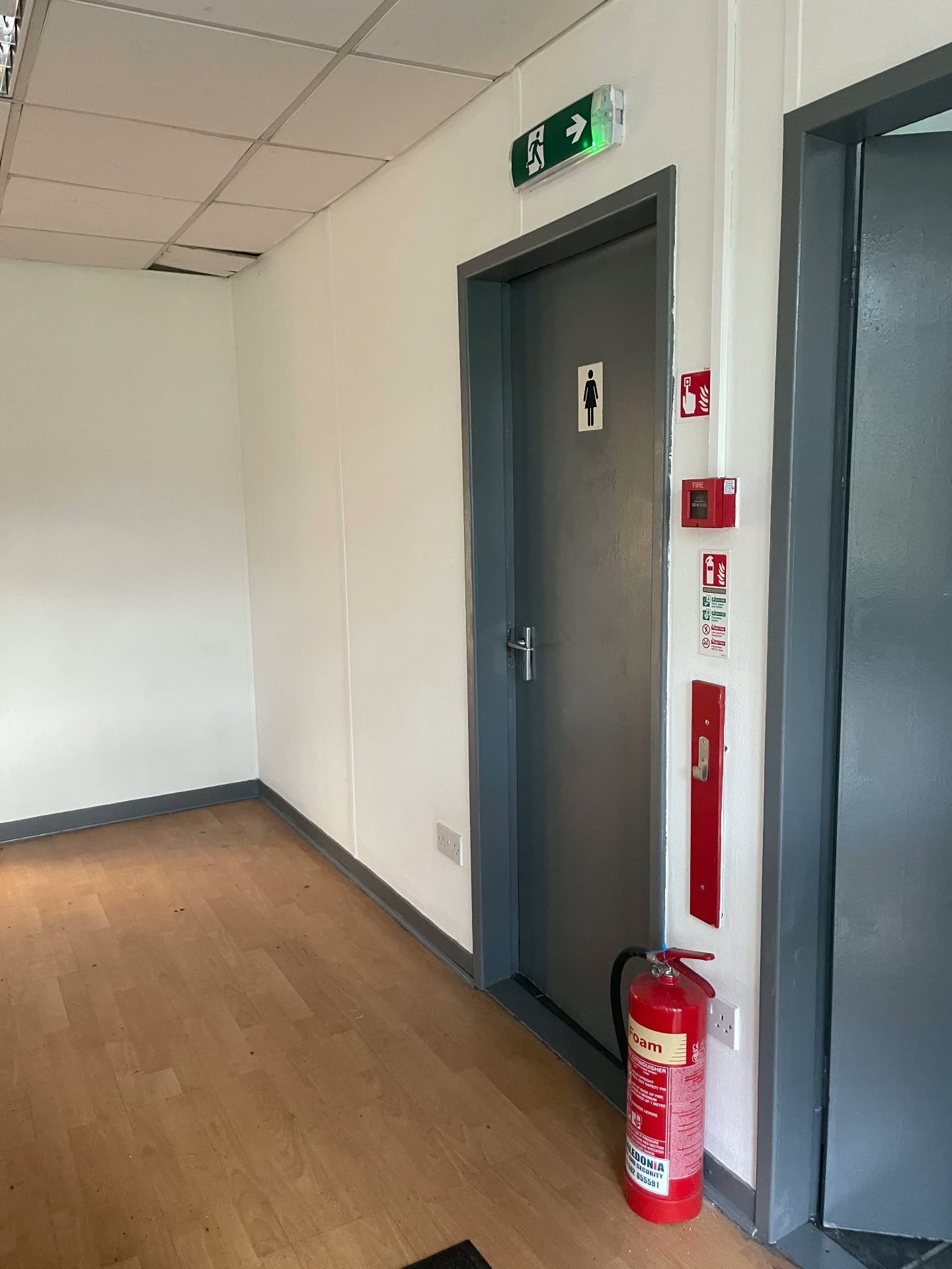 Office corridor fire door with exit signage, call point and extinguisher
